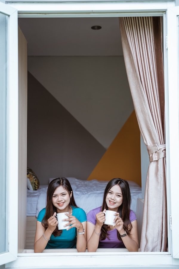 two twin Attractive asian sister holding a cup with hot tea or coffee near the window in her home